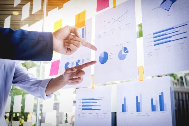 Market Entry Case. This image shows two consultants discussing pie charts and line charts posted on a conference room wall.