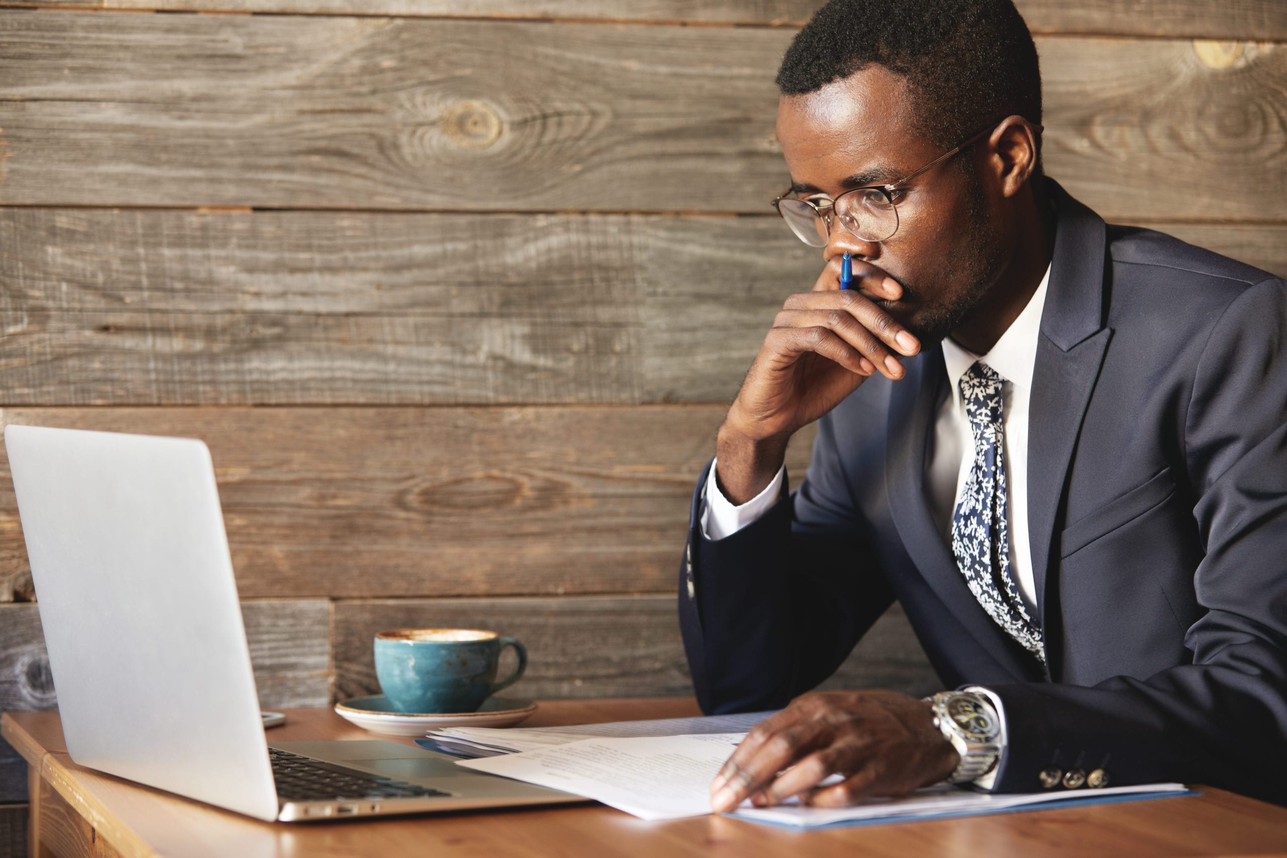 Why McKinsey? Serious African American businessman looking at laptop screen and thinking about a problem problem while sitting in coworking cafe.