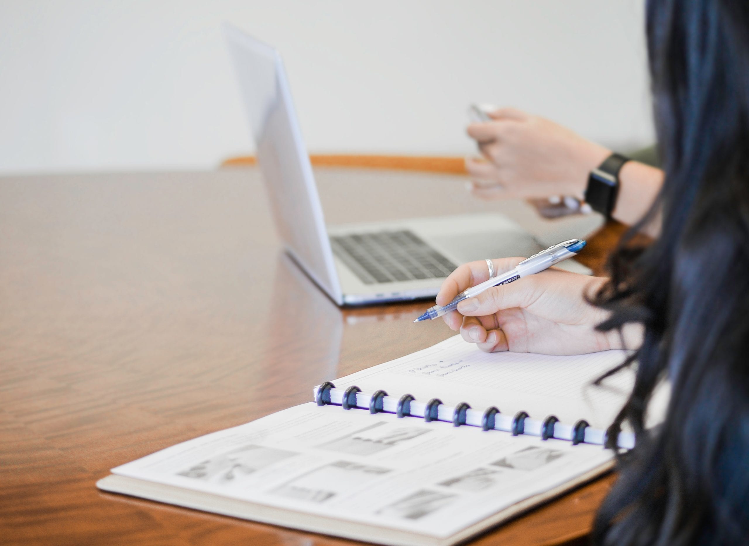 Person writing in a notebook with a laptop.