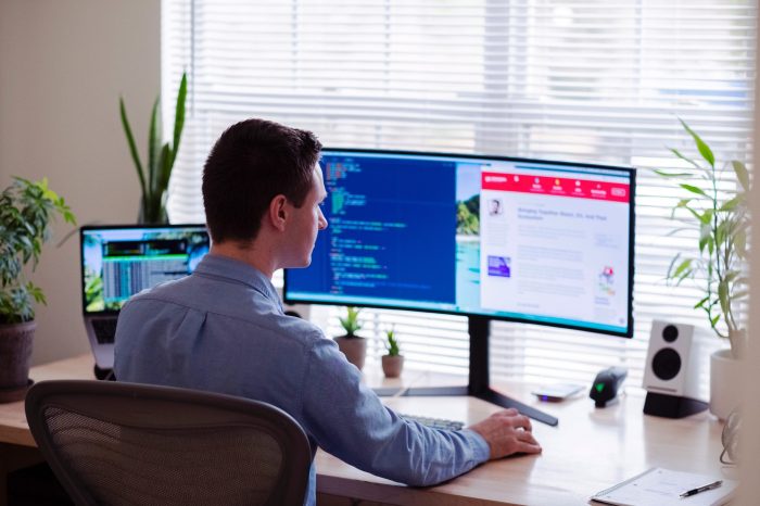 online case interview. This image shows a man in a button-down shirt sitting in his office looking at a wide-screen computer monitor.