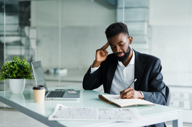 BCG Gamma Interview. This image shows a man in a suit working at a desk with a laptop and notebook.